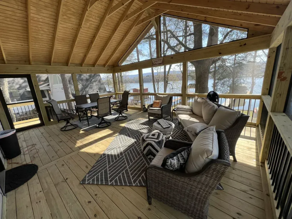 A screened in porch with a couch , chairs , table and rug.
