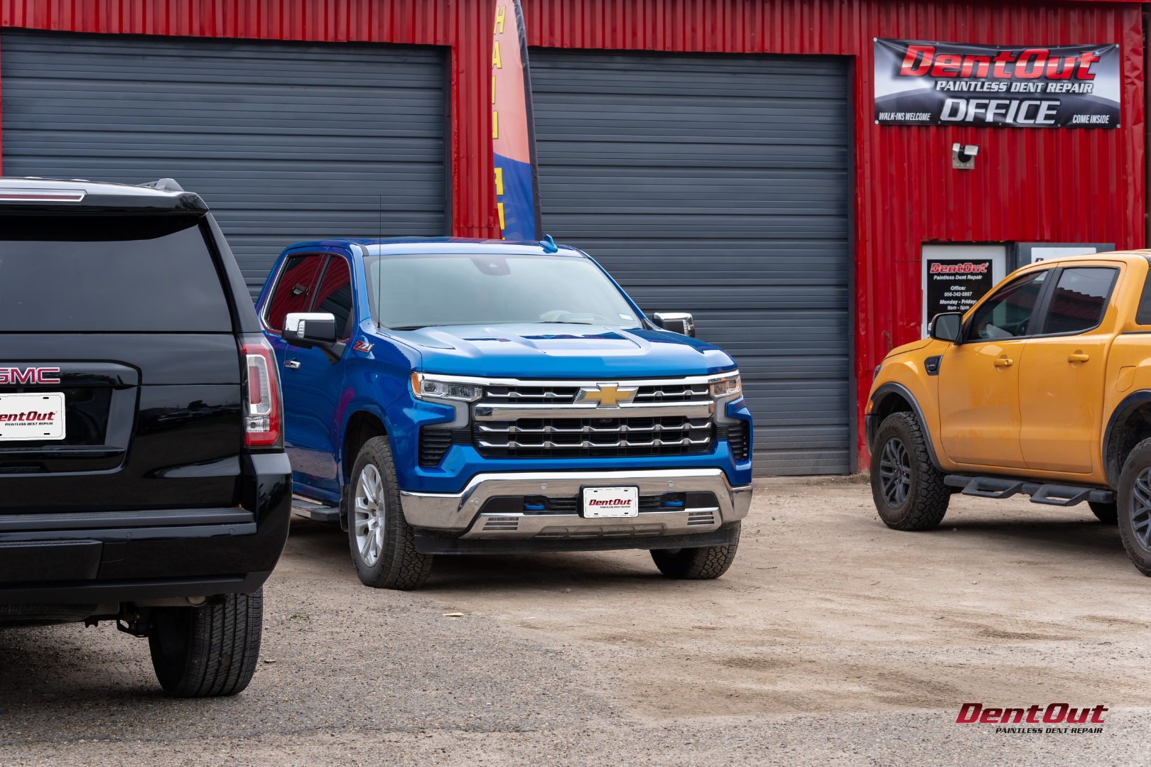 A blue suv and a yellow truck are parked in front of a garage.