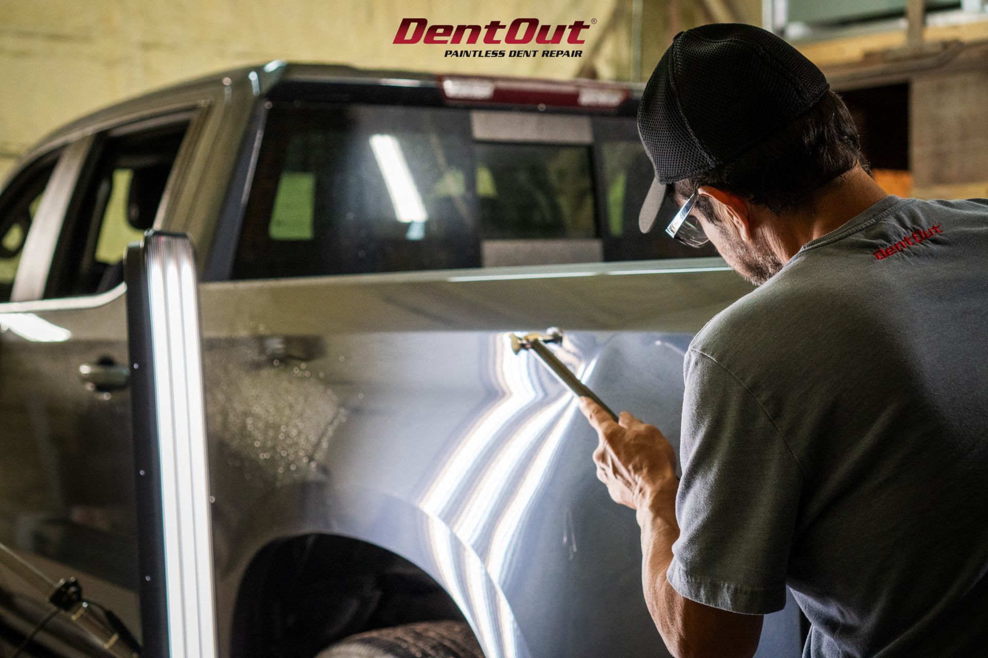 A man is working on the side of a truck with a hammer.