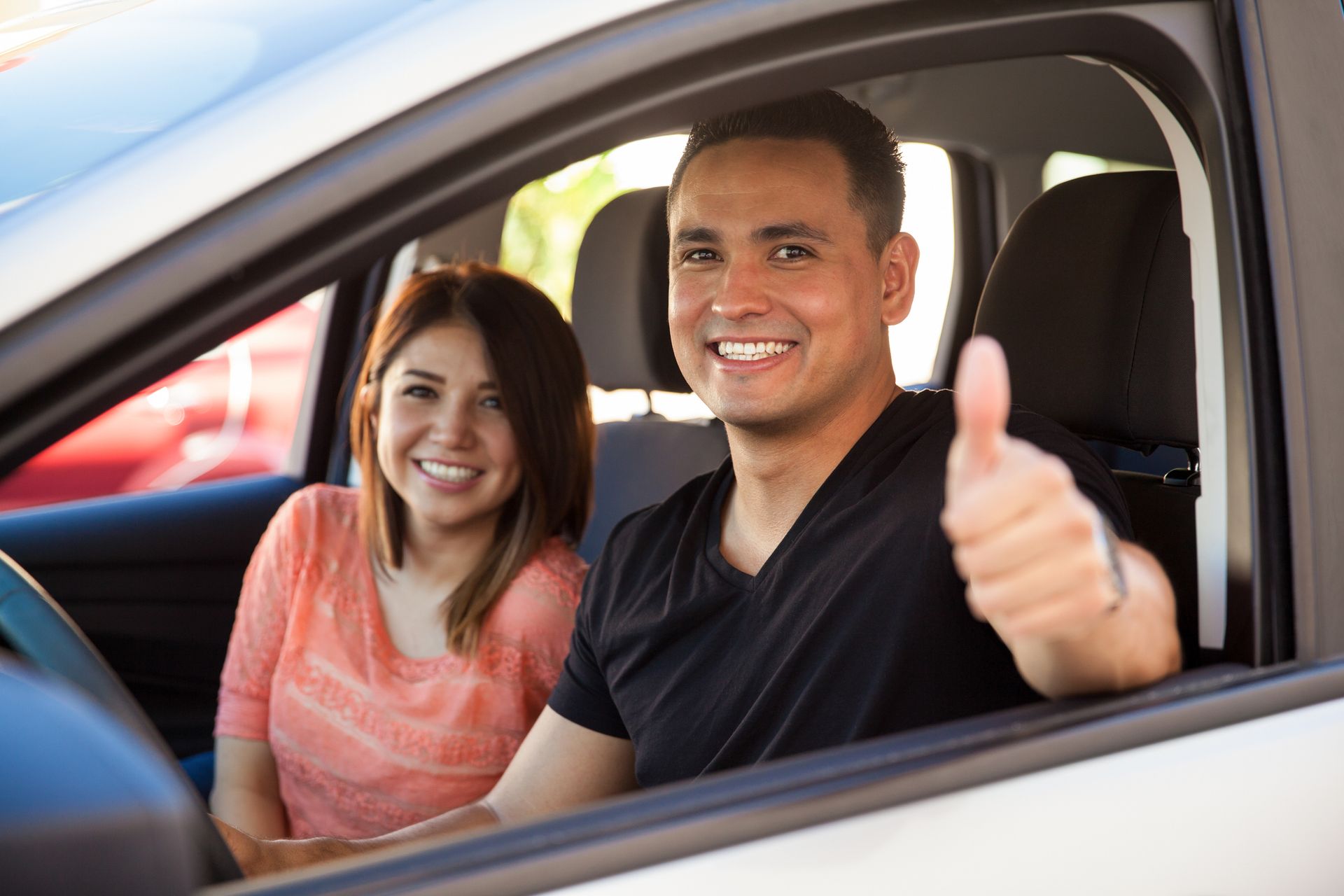 A man and a woman are sitting in a car and the man is giving a thumbs up.