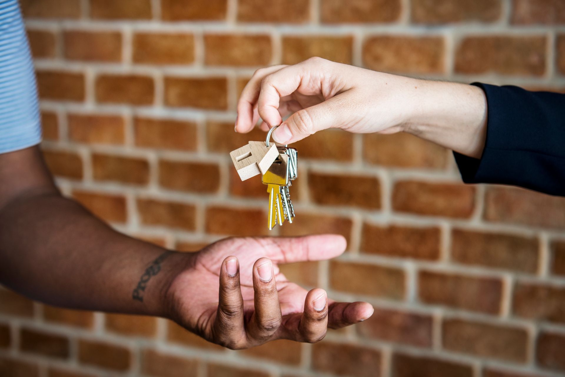 A woman is handing a man a bunch of keys in front of a brick wall.