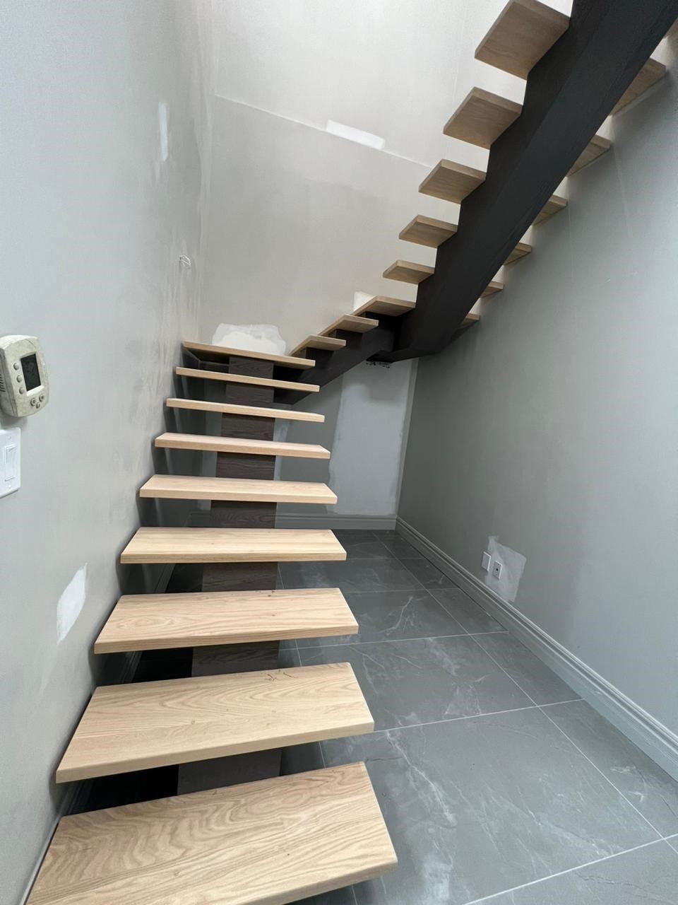 A wooden staircase in a hallway with a thermostat on the wall.