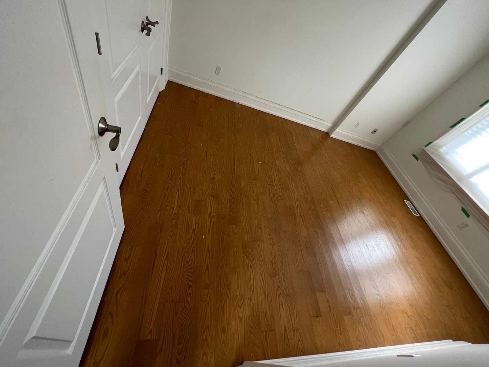 A bedroom with hardwood floors and white walls.