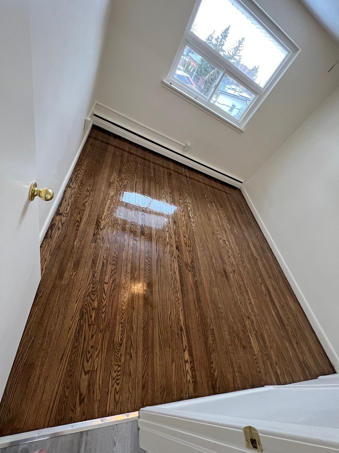 A bedroom with hardwood floors and a window.