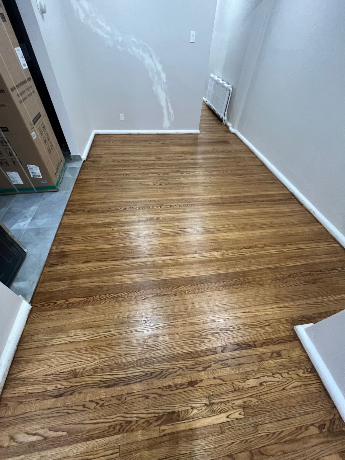 A hallway with a wooden floor and a box on the wall.