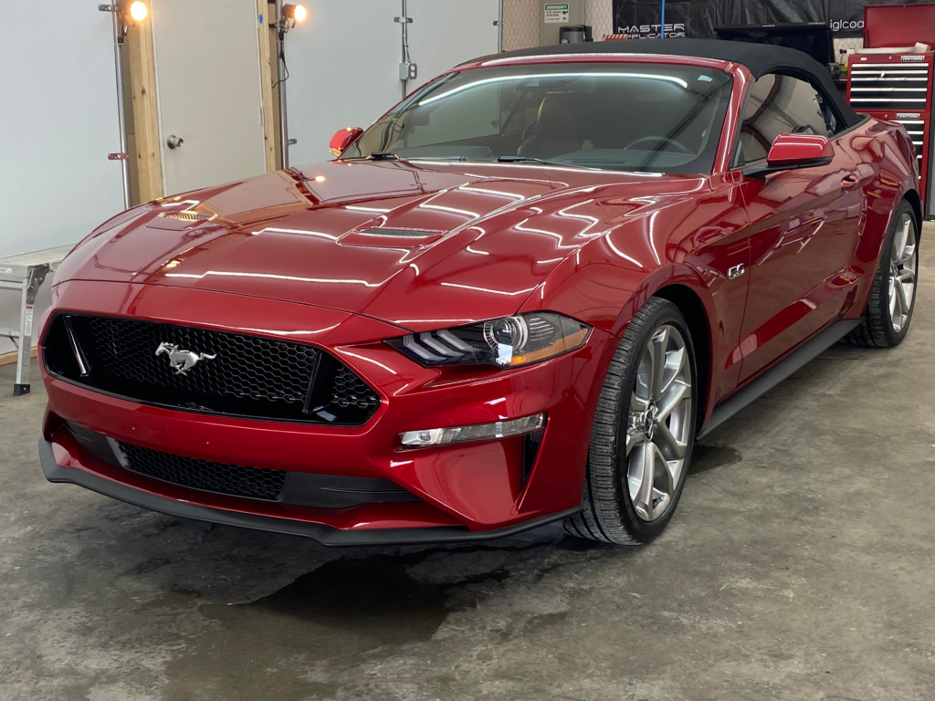 a red mustang convertible is parked in a garage .