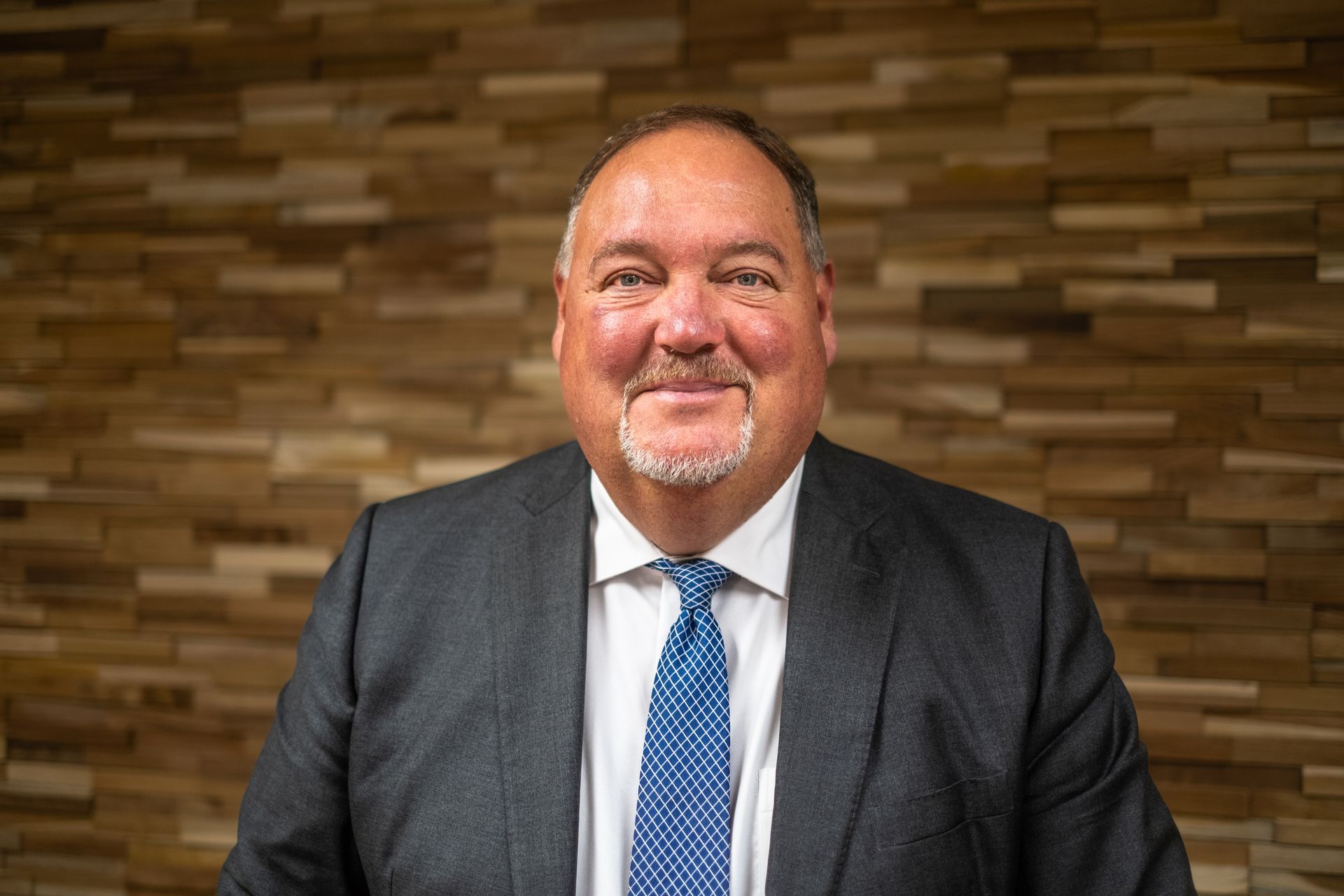 A man in a suit and tie is smiling in front of a wooden wall.