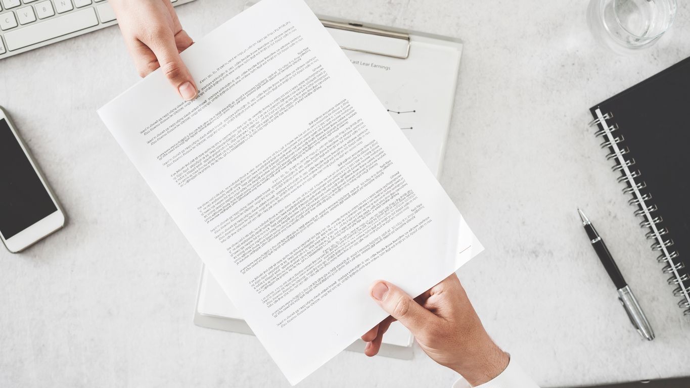 A person is holding a piece of paper over a desk.