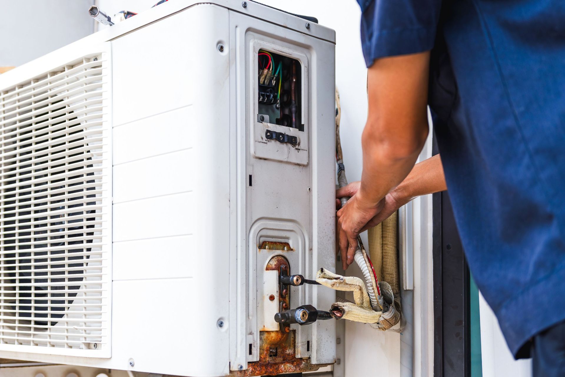 Person in blue shirt repairing an outdoor air conditioner unit.