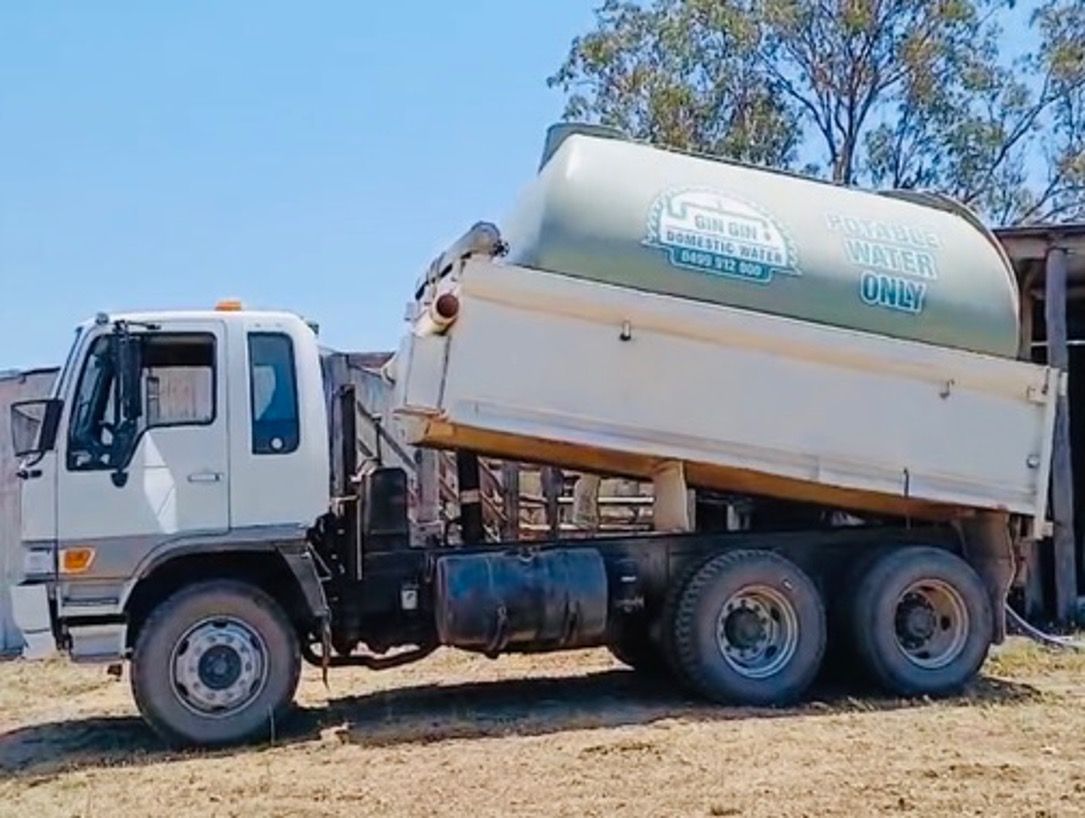 White dump truck with water tank raised, on a dirt field. — Gin Gin Domestic Water Supplies in Wallaville, QLD