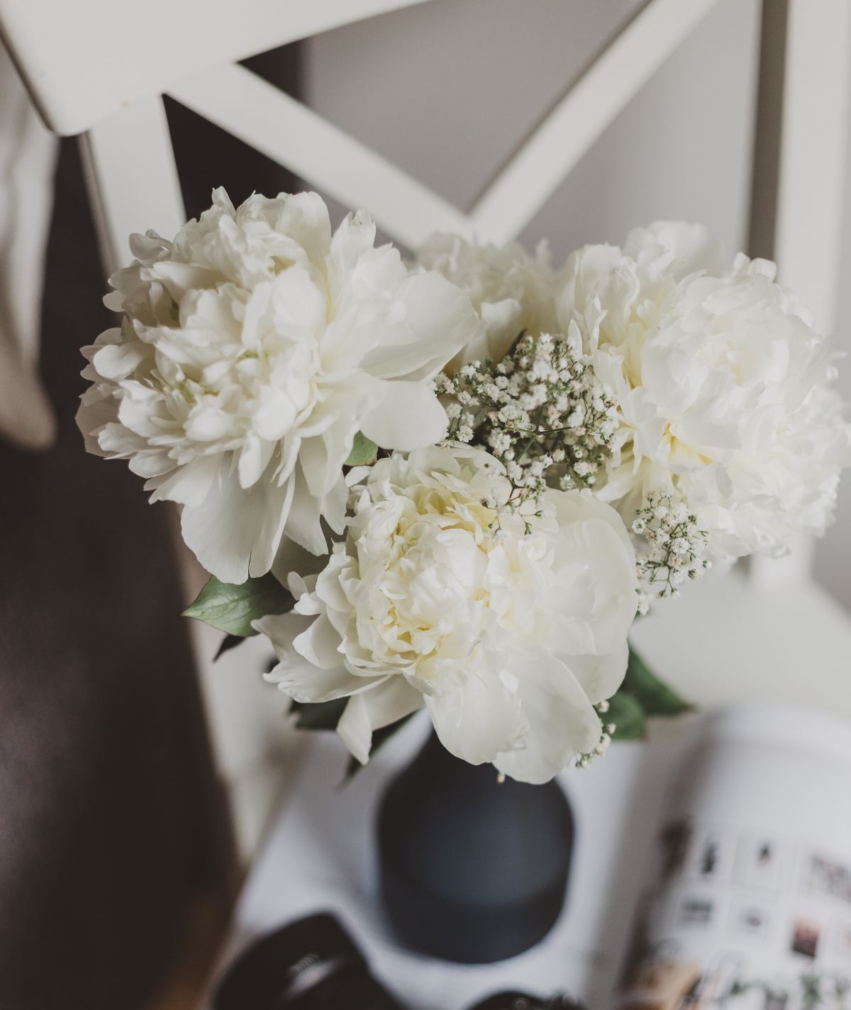 A vase filled with white flowers is sitting on a table next to a chair.
