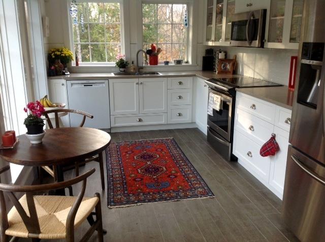 White kitchen with stainless steel appliances, wooden table, red rug.