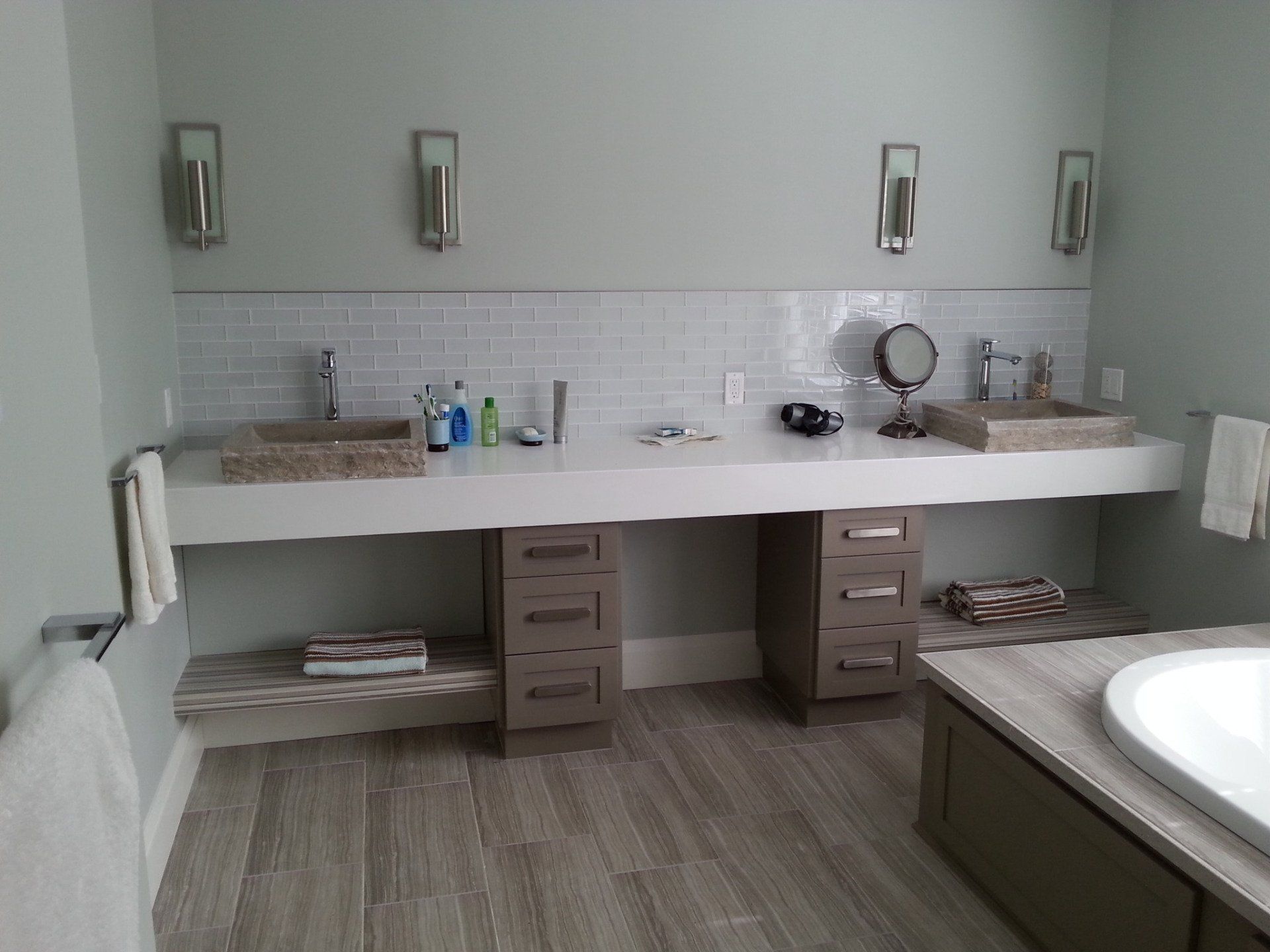 Bathroom with a long double sink vanity, white countertops, gray cabinets, and wall sconces.