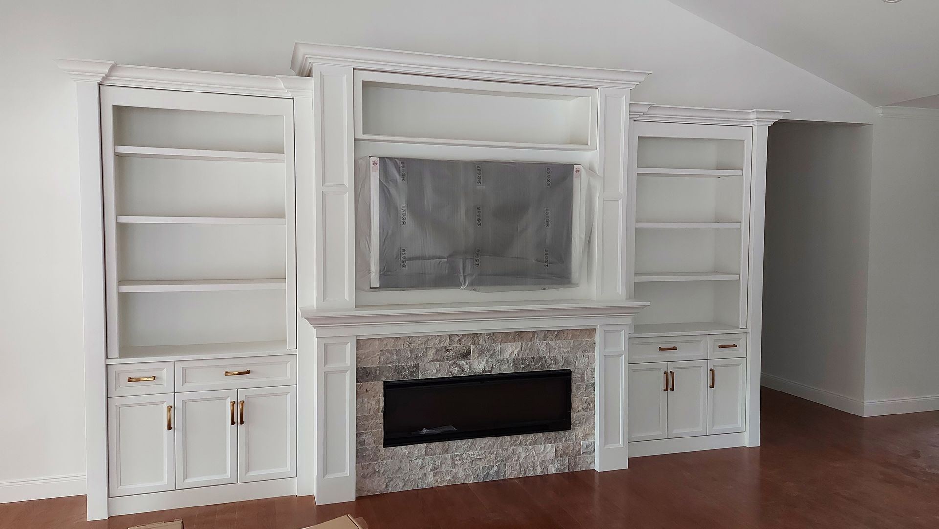 Built-in white bookcase unit with fireplace and television mount on a dark wood floor.