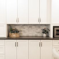 White kitchen cabinets, with a gray backsplash, and plants on a dark countertop.
