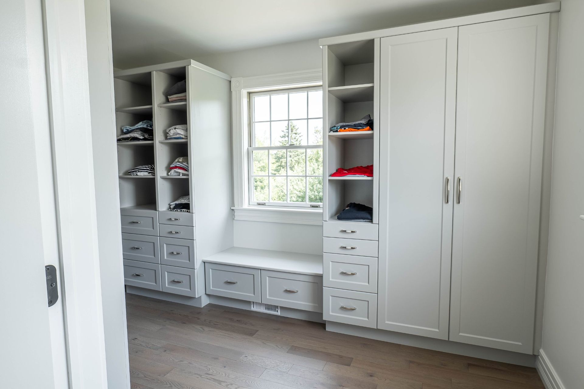A white, custom-built closet with shoe shelves, drawers, and bench seating next to a window.