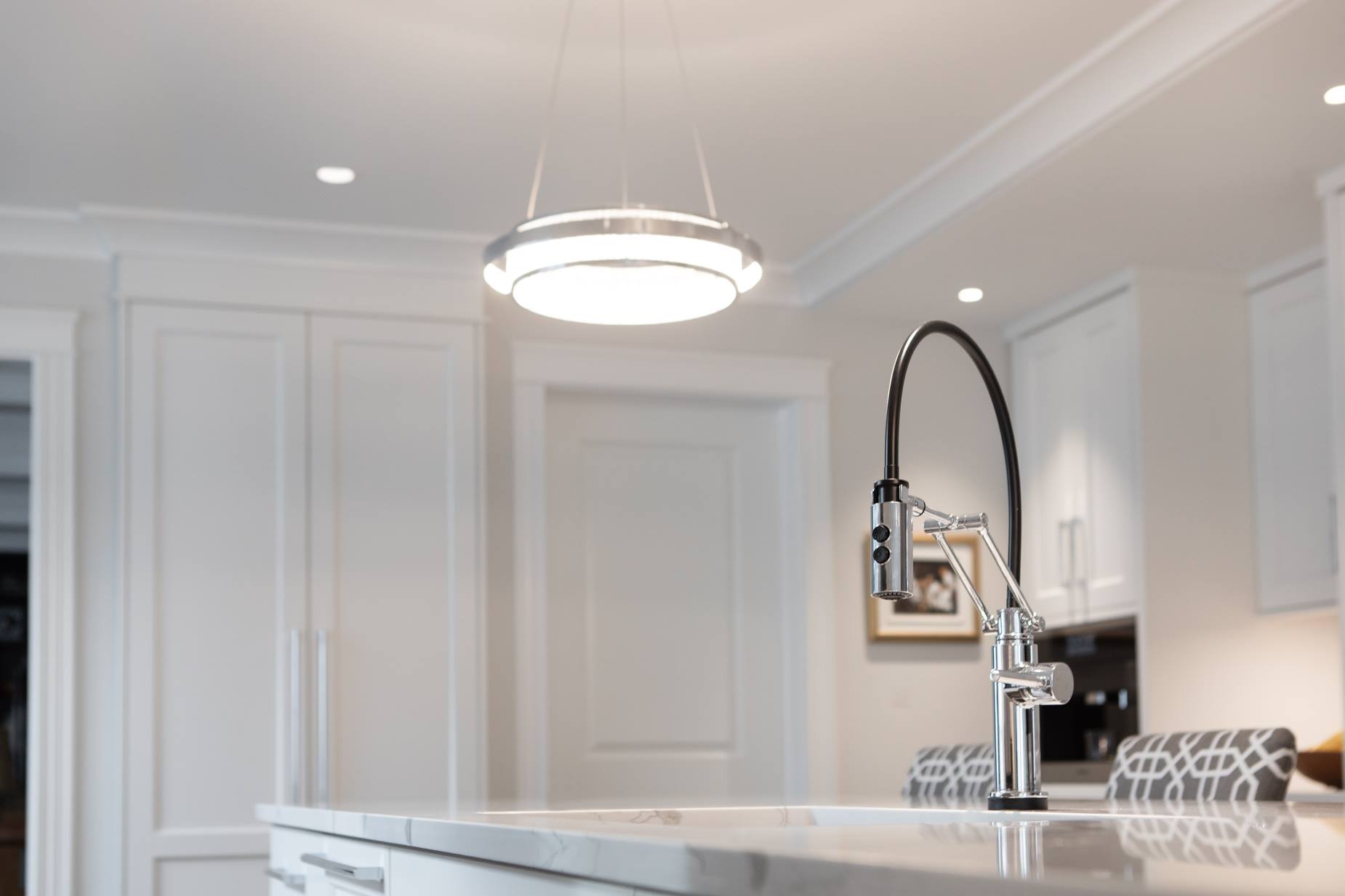 Modern kitchen with a light fixture above a sink with a tall black faucet and white cabinets.