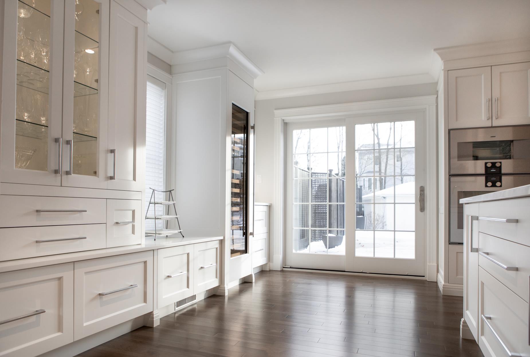 White kitchen with glass-fronted cabinets, a dark wood floor, and a sliding glass door looking out to snow.