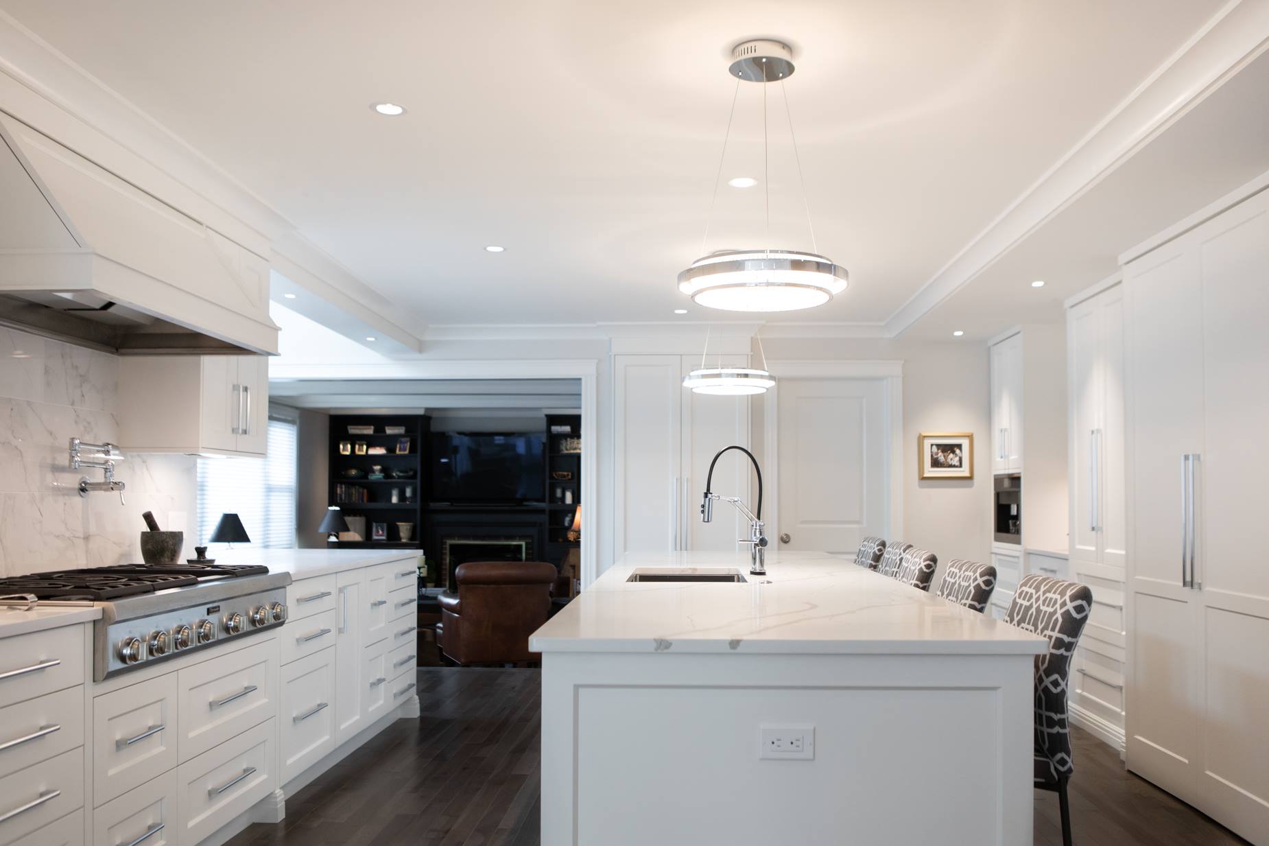 White kitchen with island and dark floors. Stainless steel appliances. View into living room.
