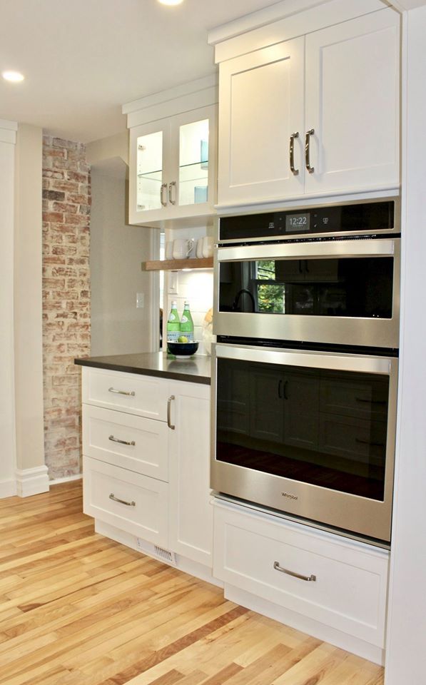 White kitchen cabinets with built-in ovens, drawers, and brick accent wall.