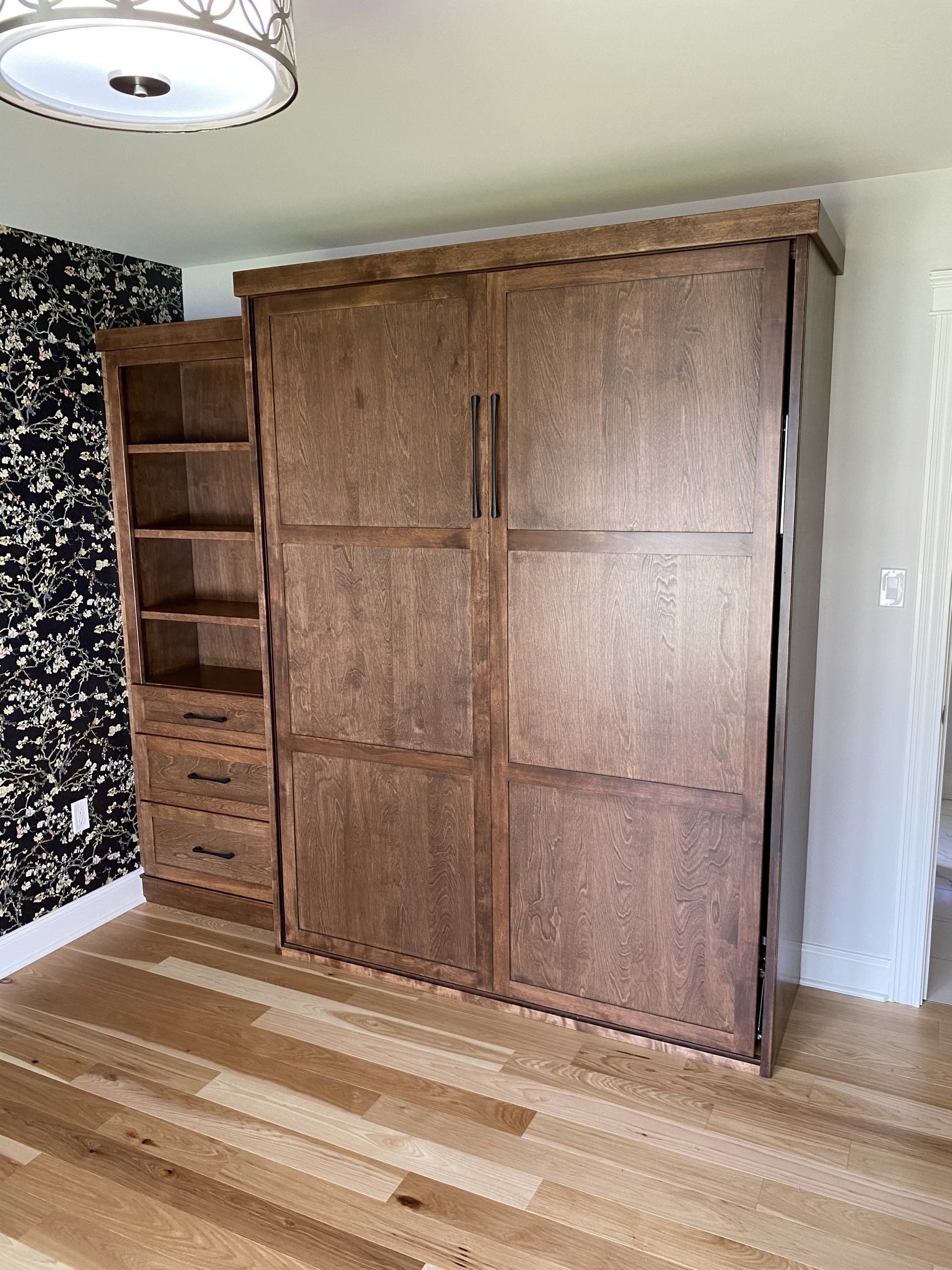 Wooden wall bed with attached bookcase in a room with wood floors.