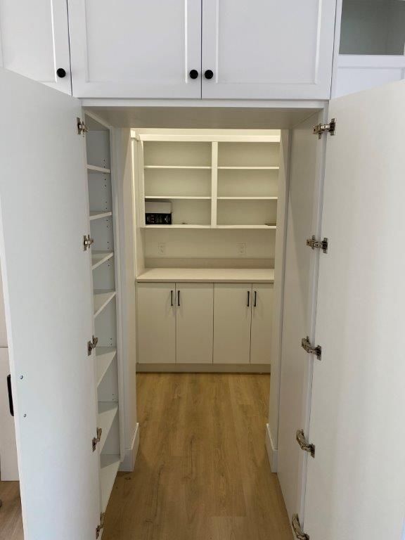 White pantry with shelves, cabinets, and wooden floor, viewed from the doorway.