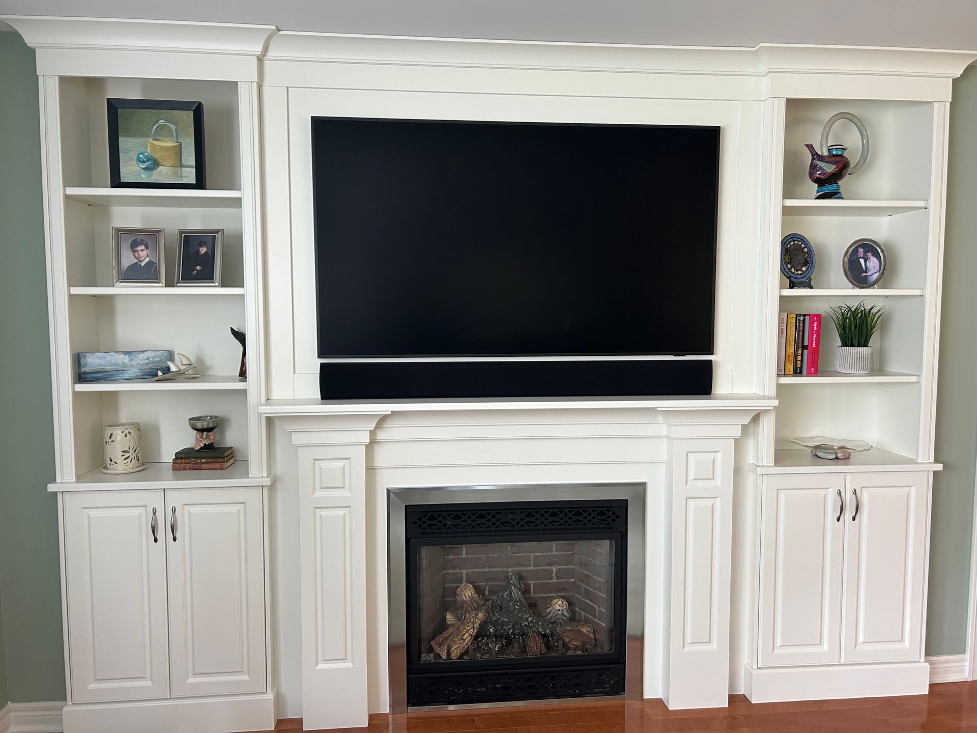 White built-in entertainment center with TV over fireplace and flanking bookshelves displaying decor.