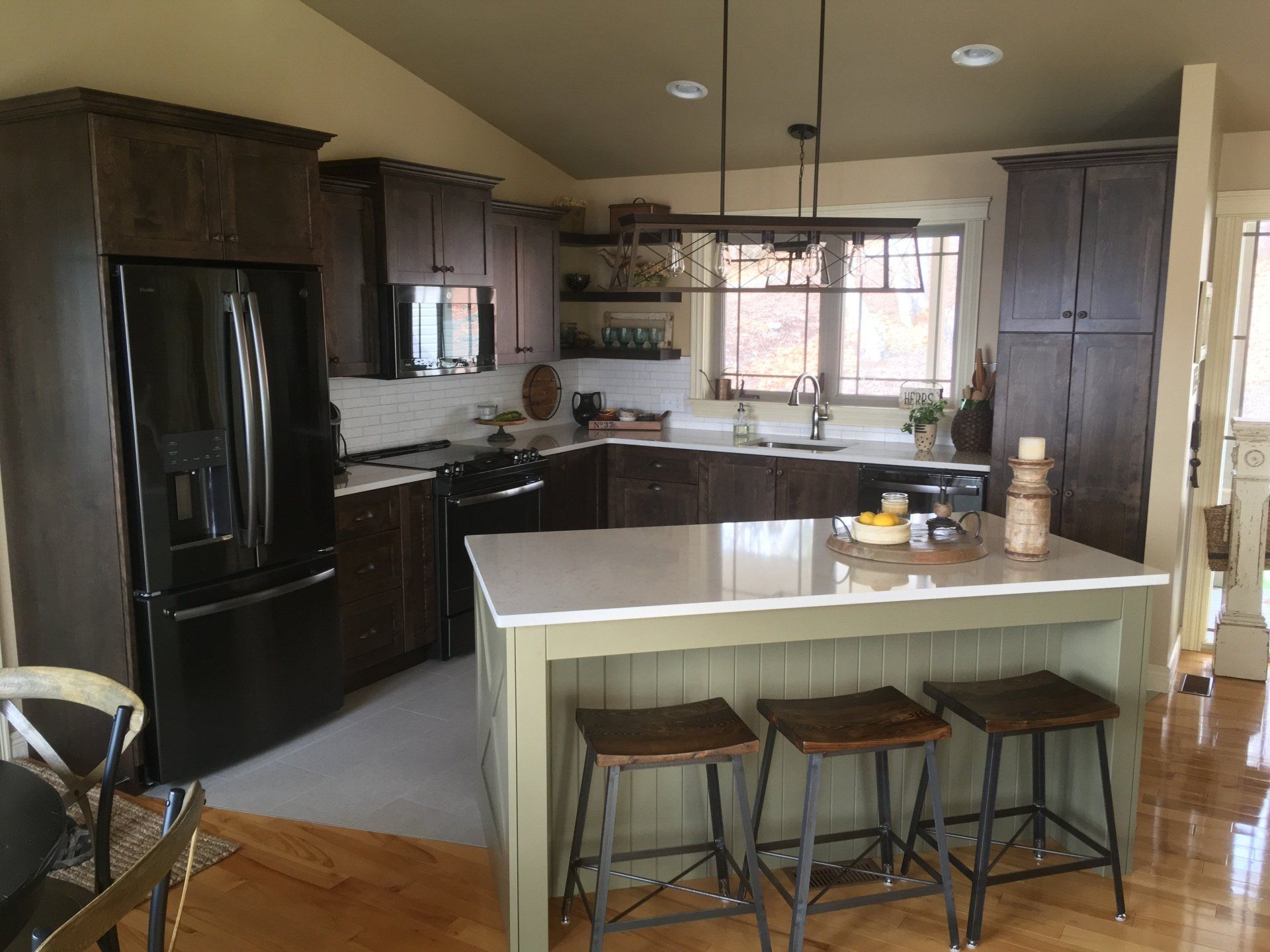Modern kitchen with dark wood cabinets, stainless steel appliances, and a green island with stools.