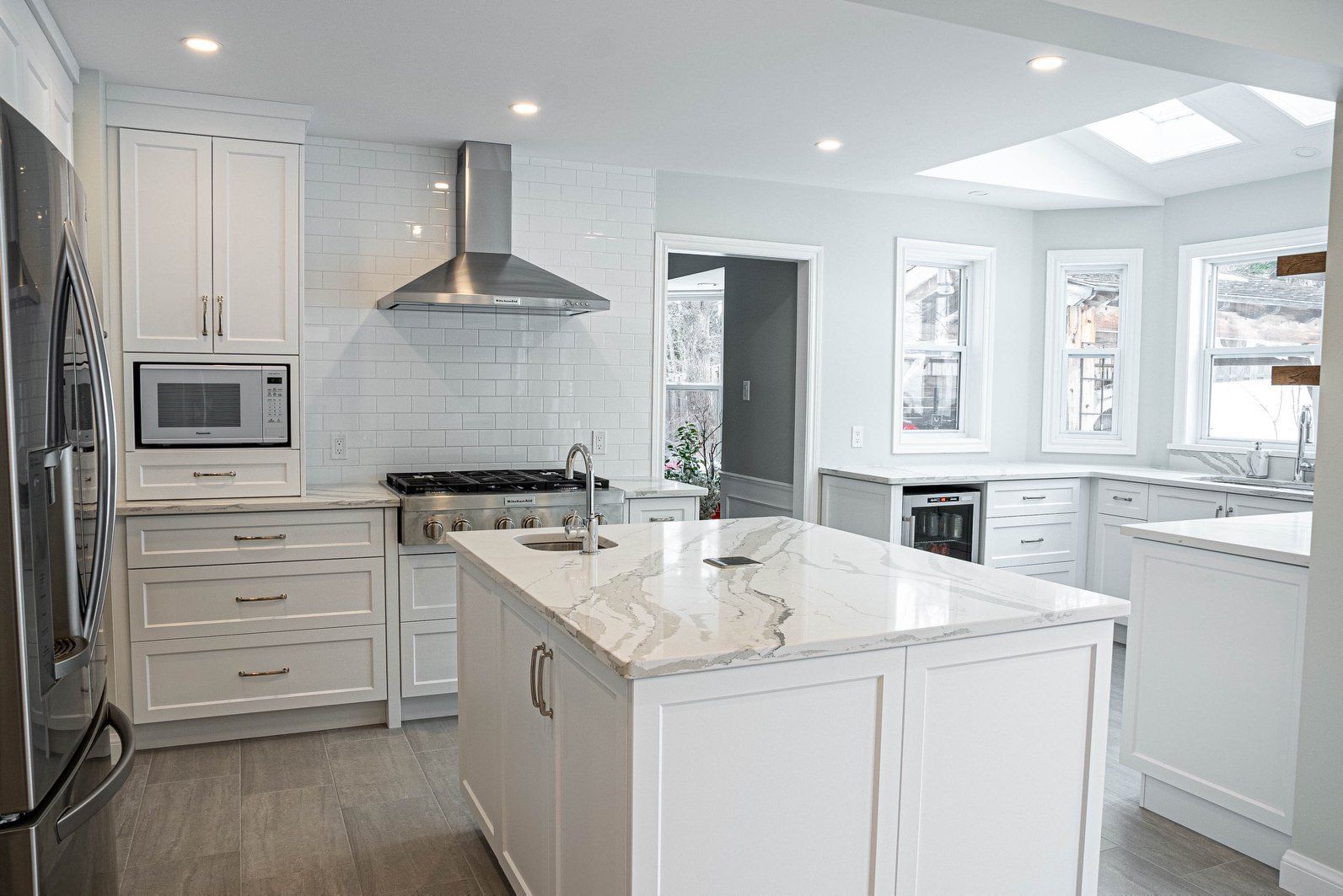 Modern white kitchen with island, stainless steel appliances, and natural light.
