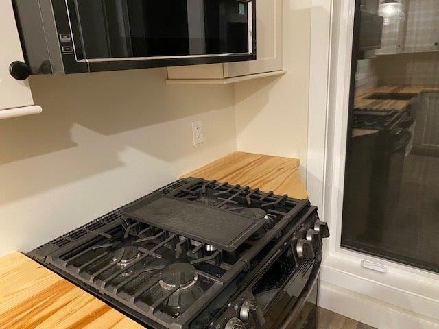 Gas stove in a kitchen with a microwave above and a window to the right.