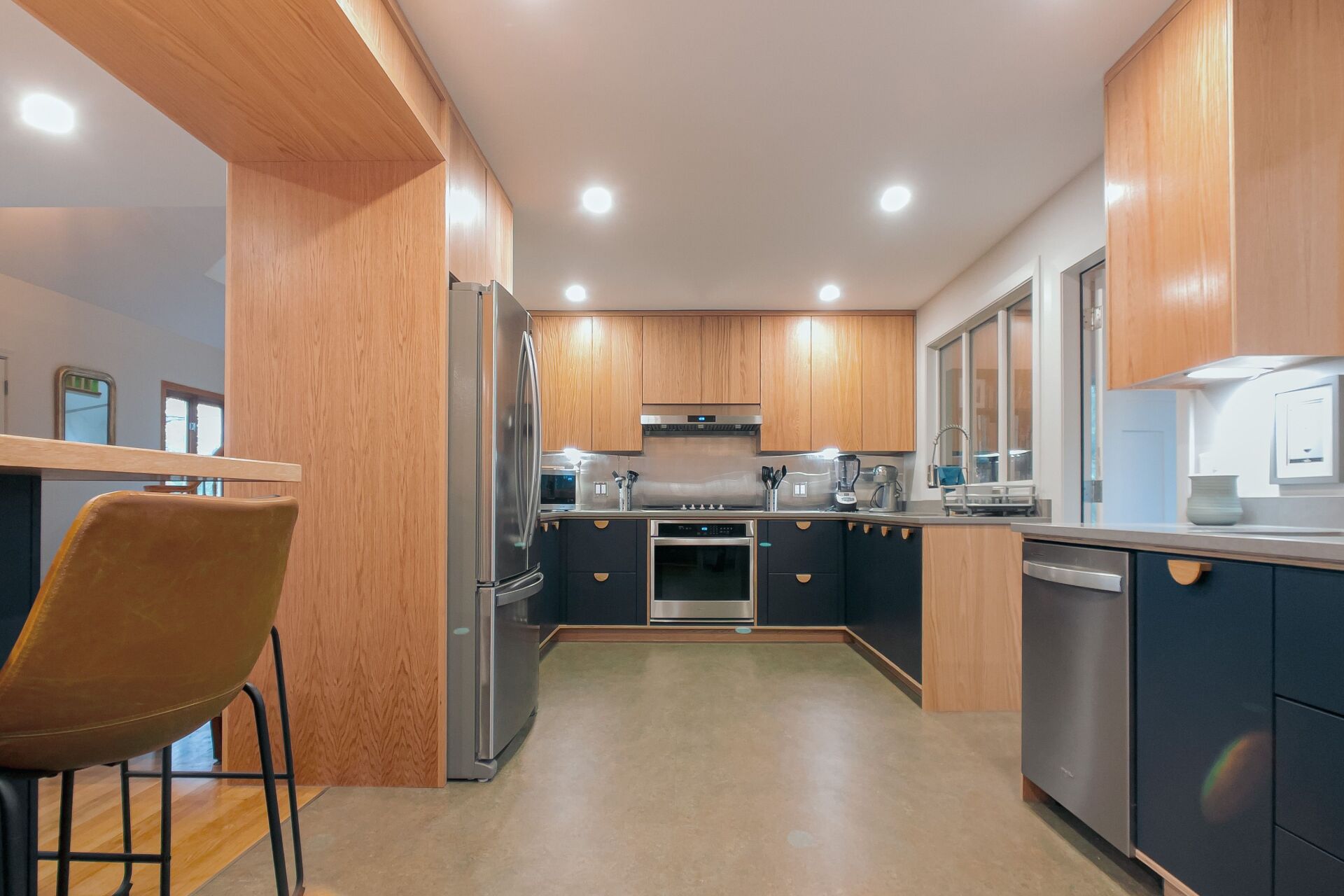 Modern kitchen with light wood cabinets, navy blue lower cabinets, stainless steel appliances.