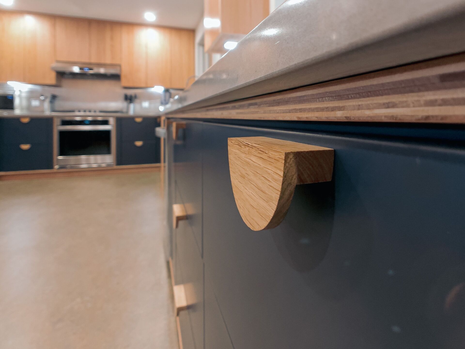 Close-up of a blue kitchen cabinet with a wooden half-moon handle.