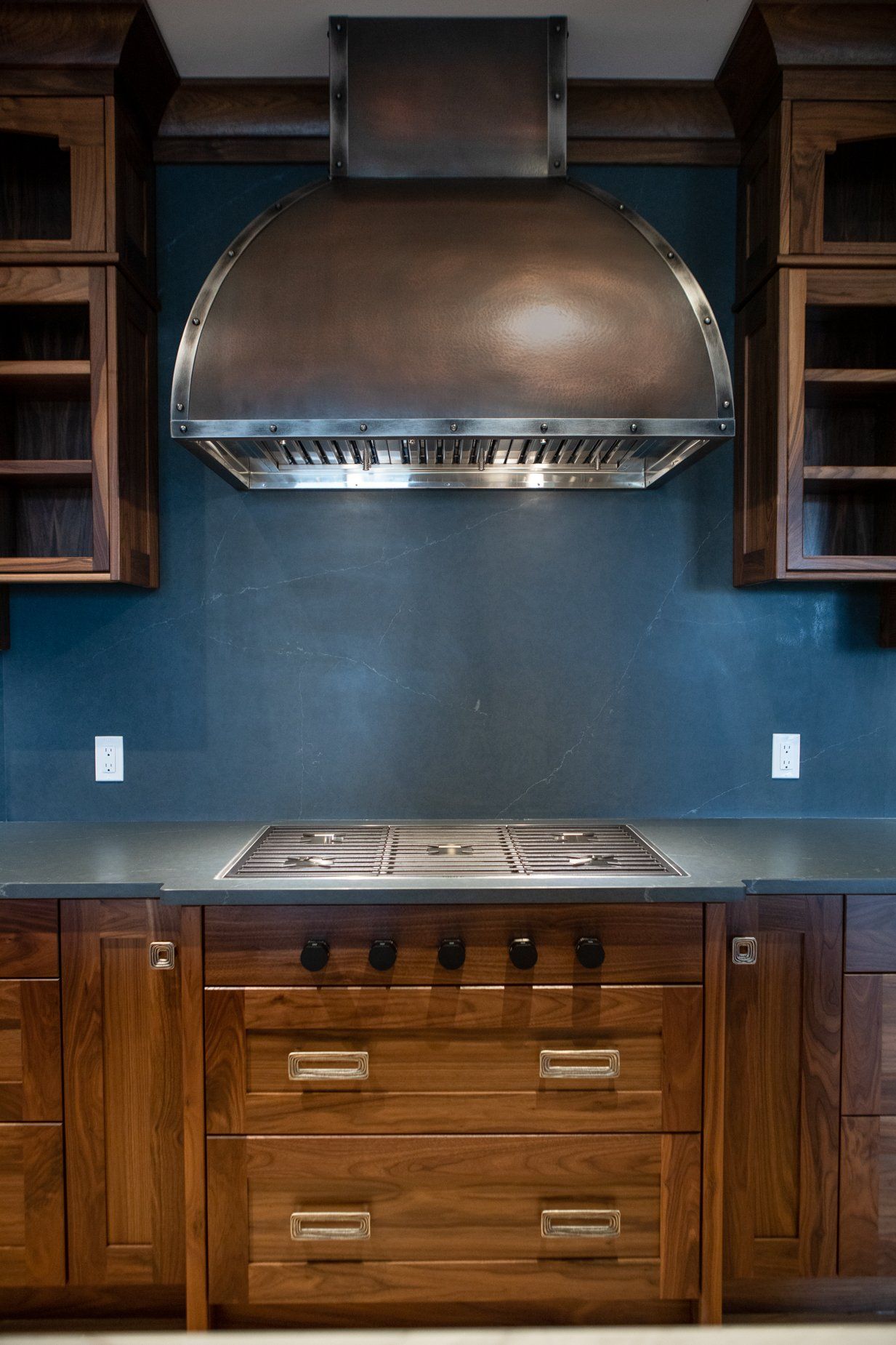 Kitchen with a stainless steel range hood over a stovetop, framed by wooden cabinets on a blue wall.