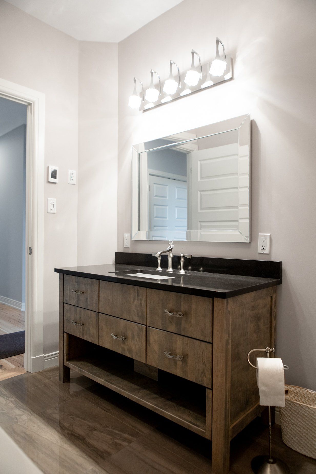 Bathroom with wood vanity, black countertop, mirror, and light fixture. Dark wood floor.