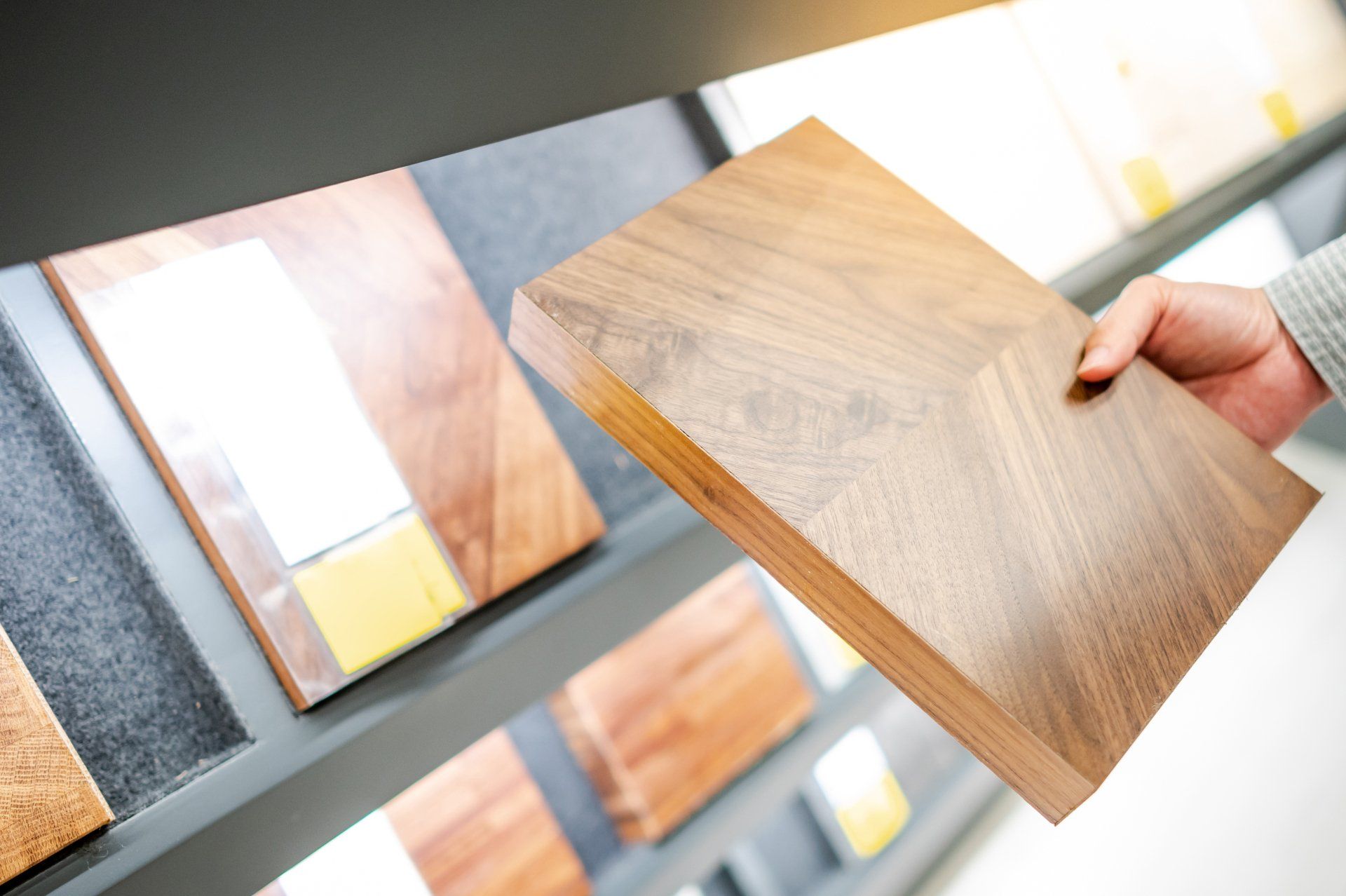 Person holding a sample of dark brown wood, comparing it to wood samples on display.