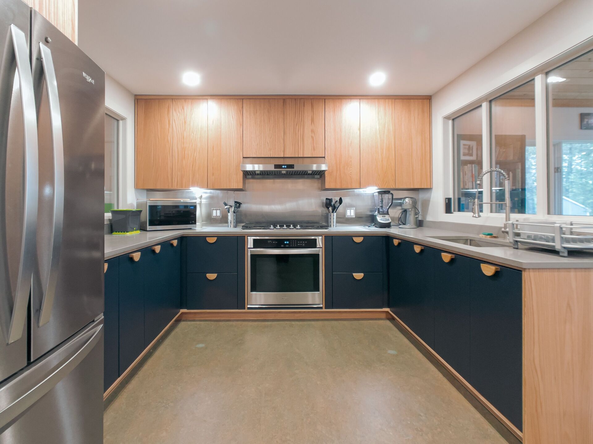 U-shaped modern kitchen with navy blue and wood cabinets, stainless steel appliances, and light brown flooring.