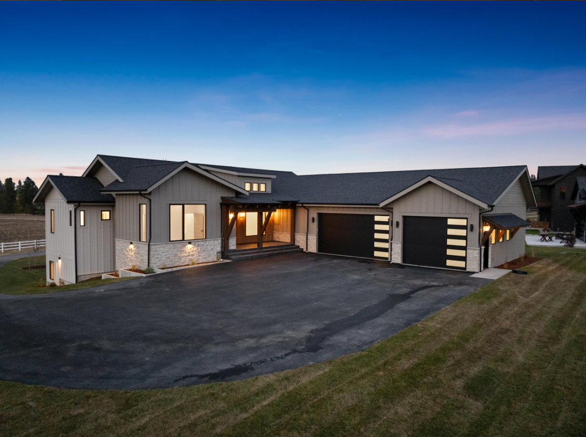 A large house with two garages is sitting on top of a lush green field.