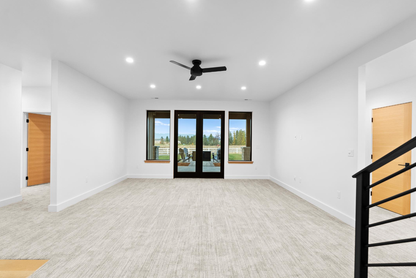 An empty living room with a ceiling fan and sliding glass doors.