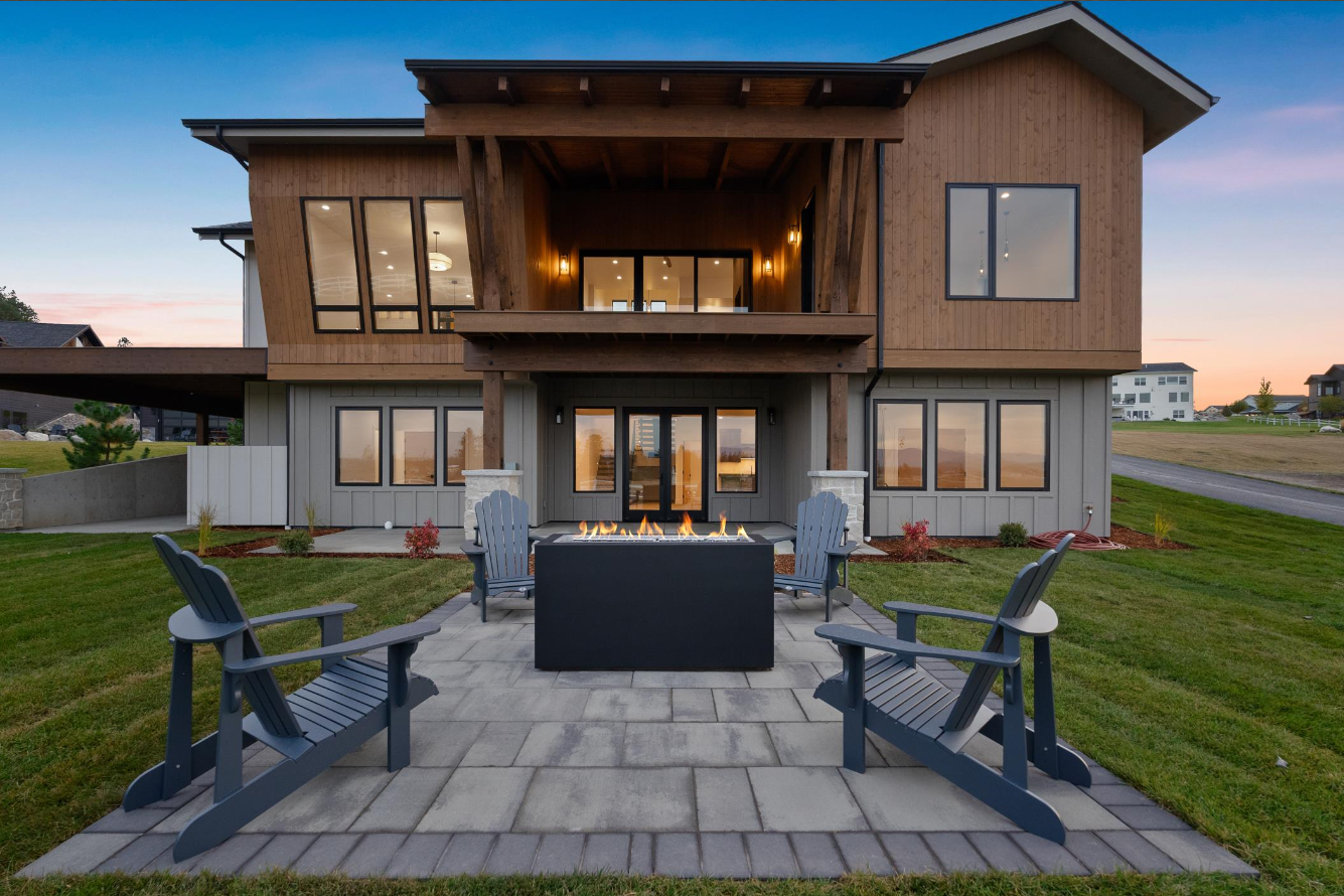 A large house with a fire pit and chairs in front of it.