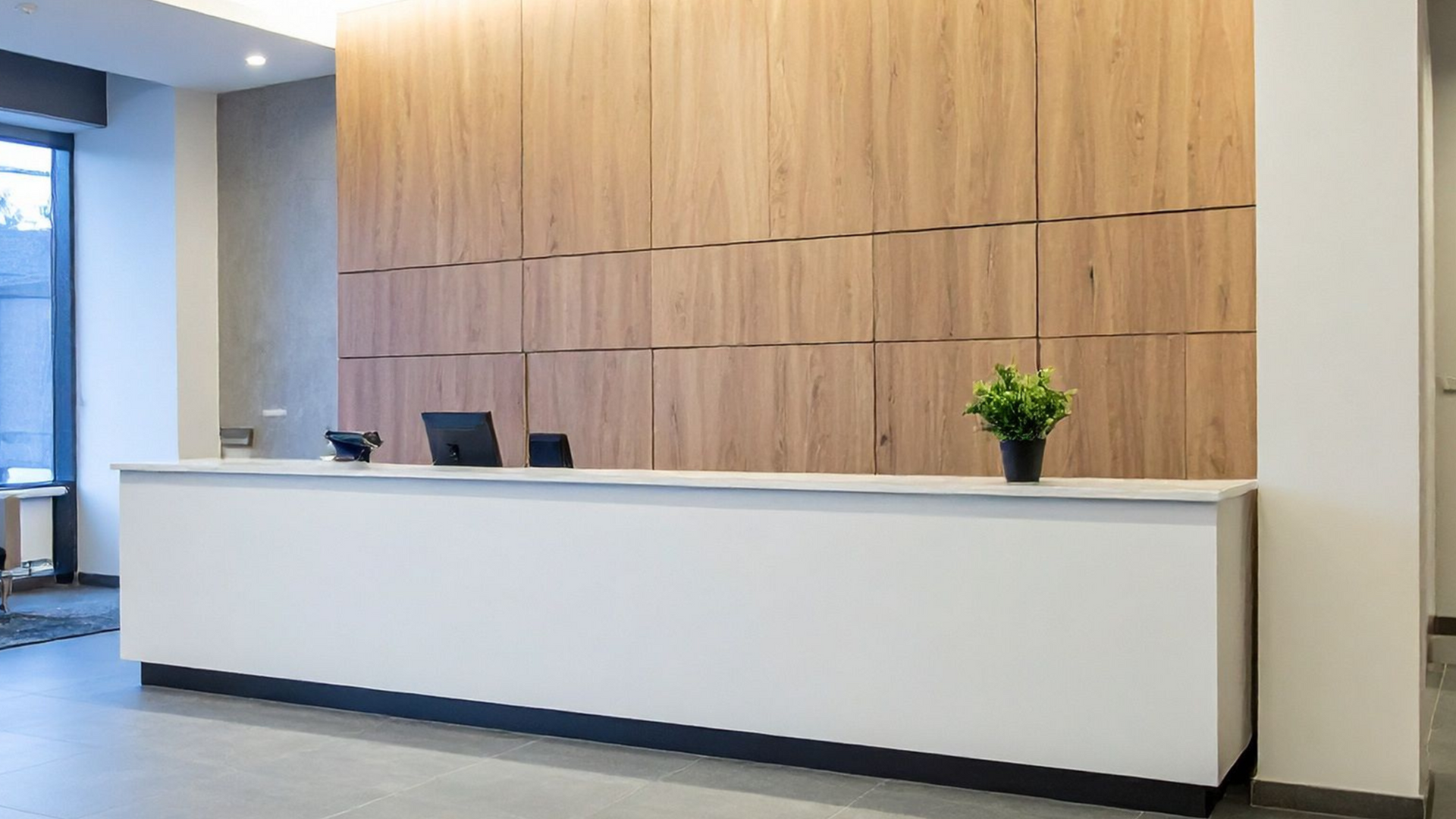 Modern white and wood reception desk with a plant and computer.