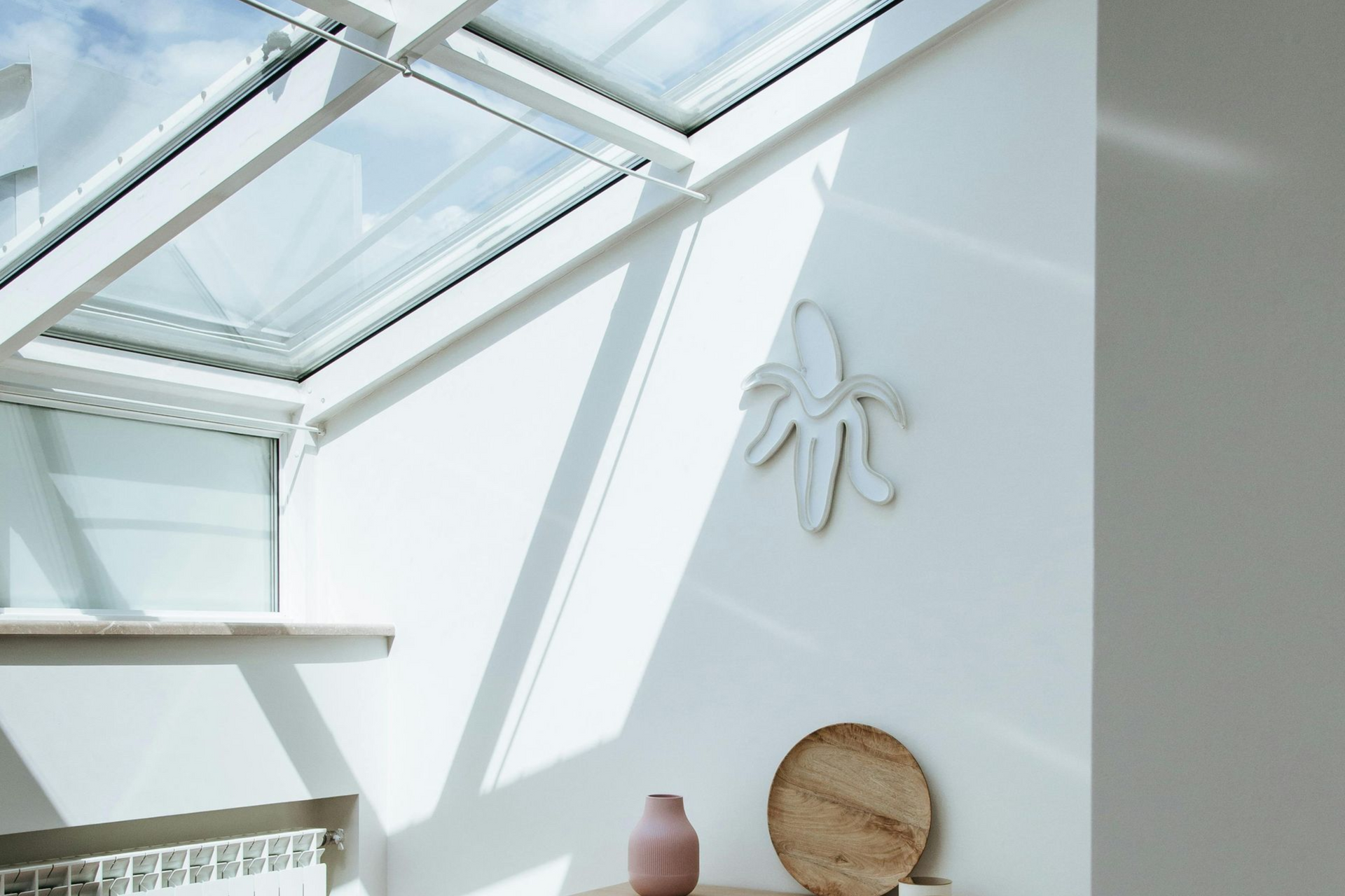 Bright interior with skylight and banana-shaped wall art. Shadow play, neutral tones.