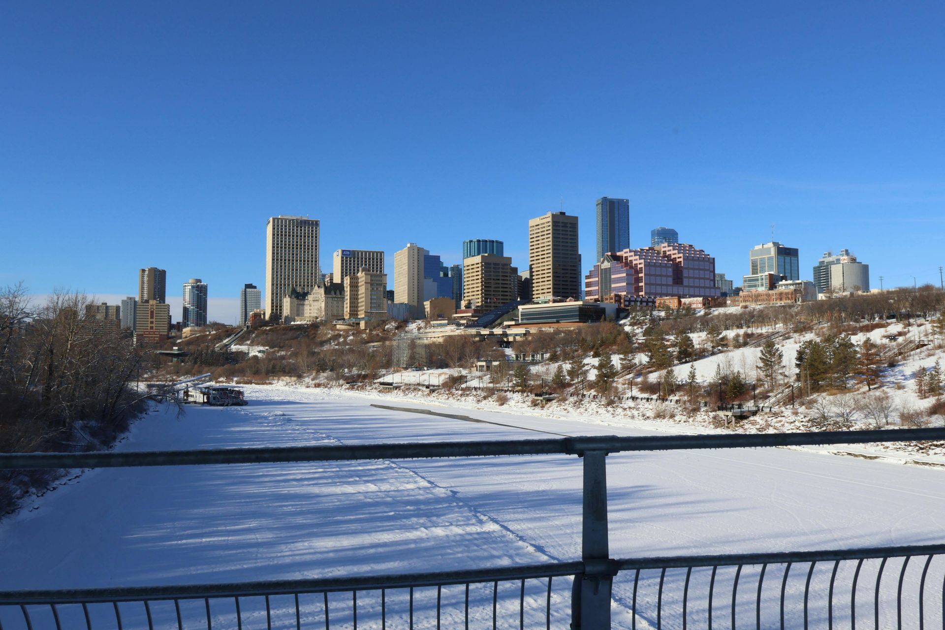 City skyline on a bright, sunny day, with a snow-covered river in the foreground.