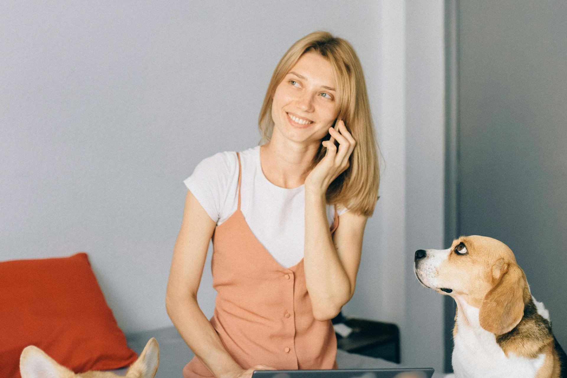 Woman smiling while on the phone, a beagle dog looking up at her indoors.