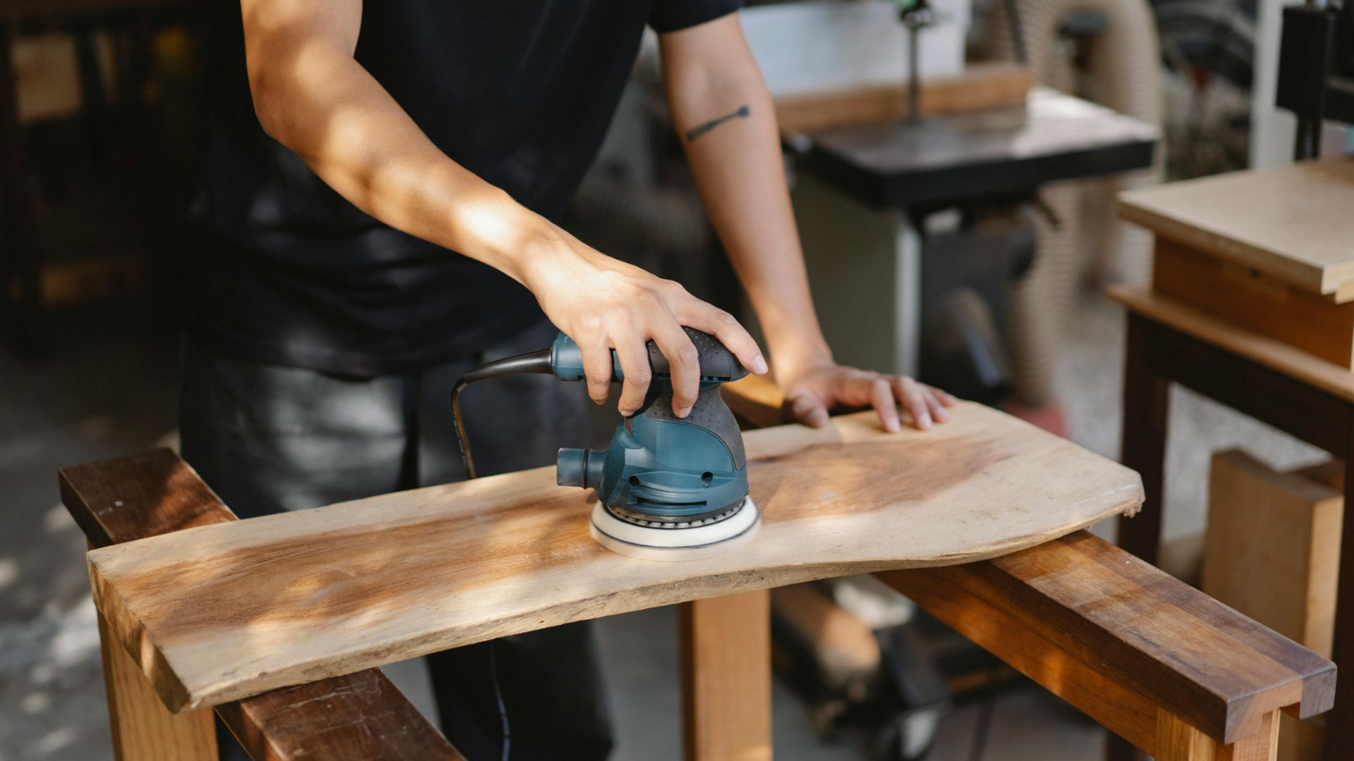 Person sands wood with a power sander on a workbench.