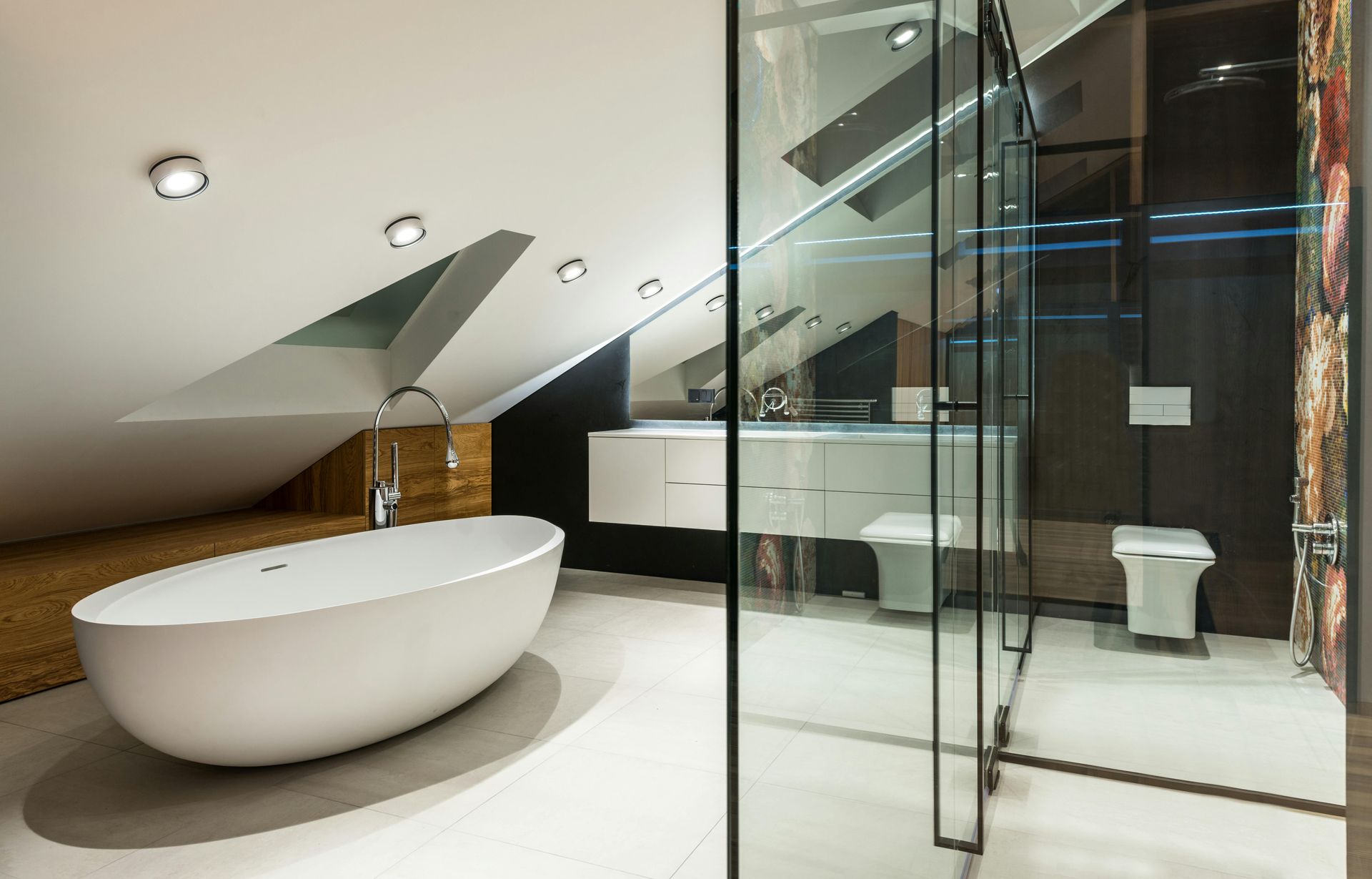 Modern bathroom with oval tub, white vanity, glass shower, and sloped ceiling.