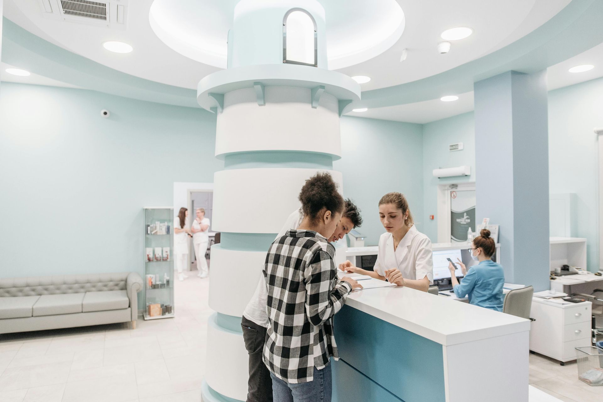 Patients checking in at a reception desk in a clinic, featuring a lighthouse-themed design with light blue and white.