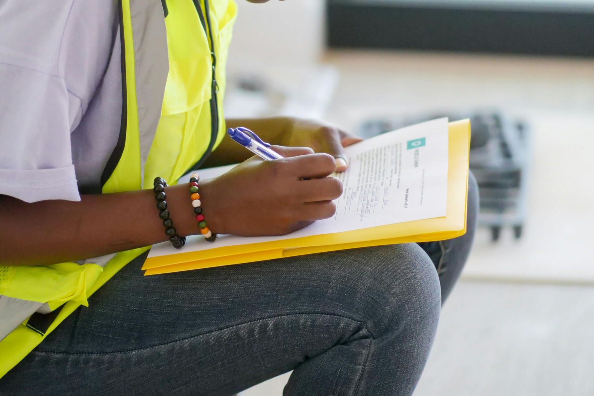Person in reflective vest writing on a clipboard, possibly on a construction site.
