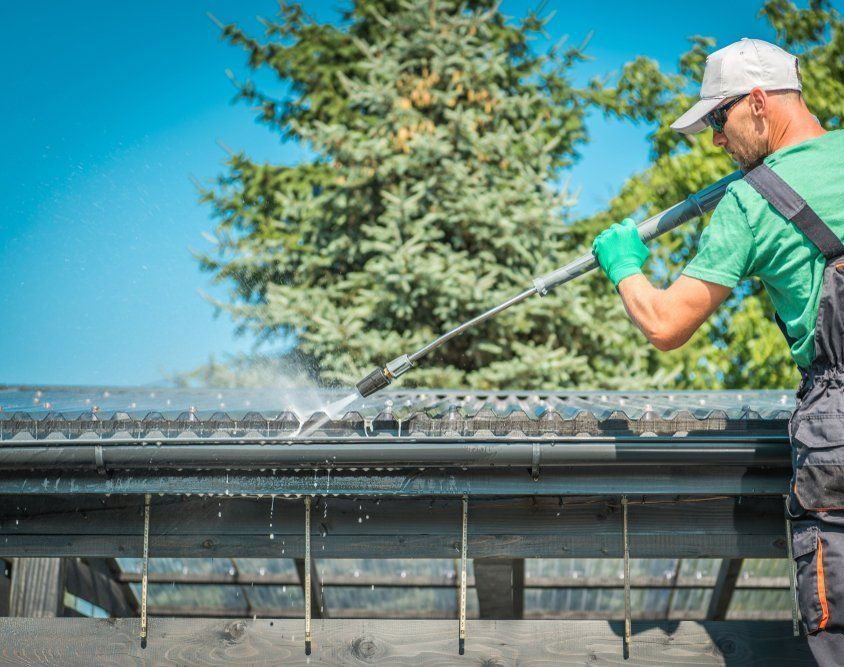 A Person in a Green Shirt and Work Overalls Pressure Washes — South Coast Pressure Washer in Albion Park, NSW