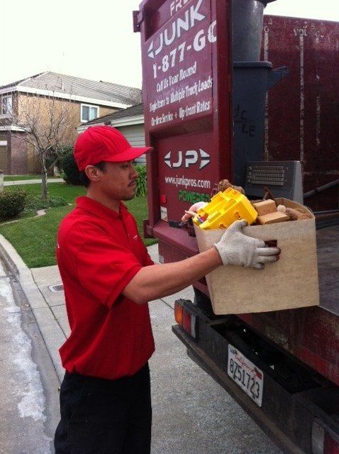 A man in a red shirt holds a box in front of a junk truck