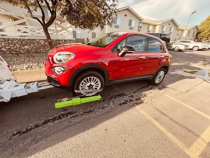 A red Fiat 500X SUV being towed by a truck in a parking lot on a sunny day.